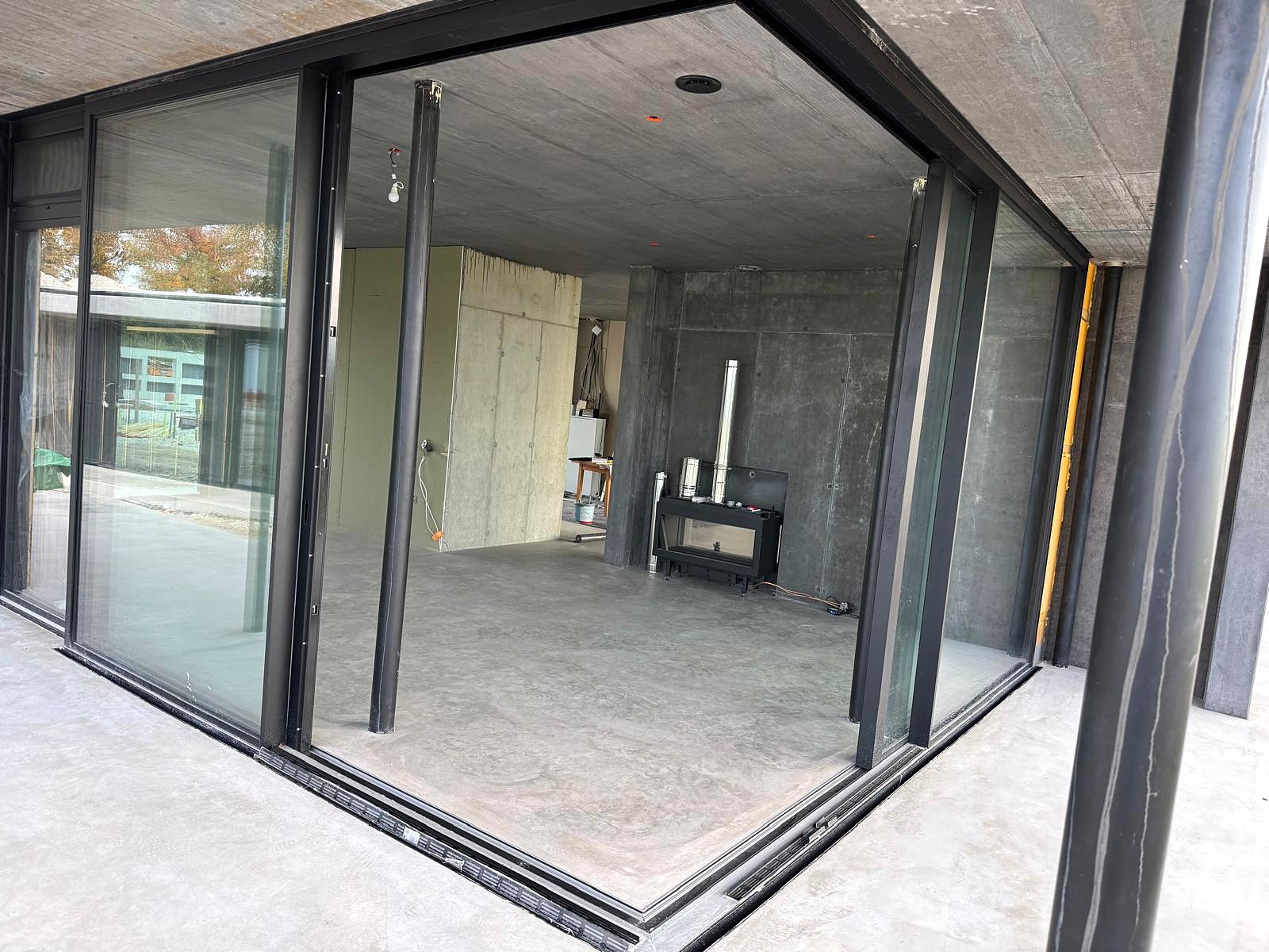 Aluminium-Schiebefenster an einem Neubau im Rohbau, Eckbereich komplett geöffnet, Blick in den Wohnraum mit Sichtbeton, Oberösterreich