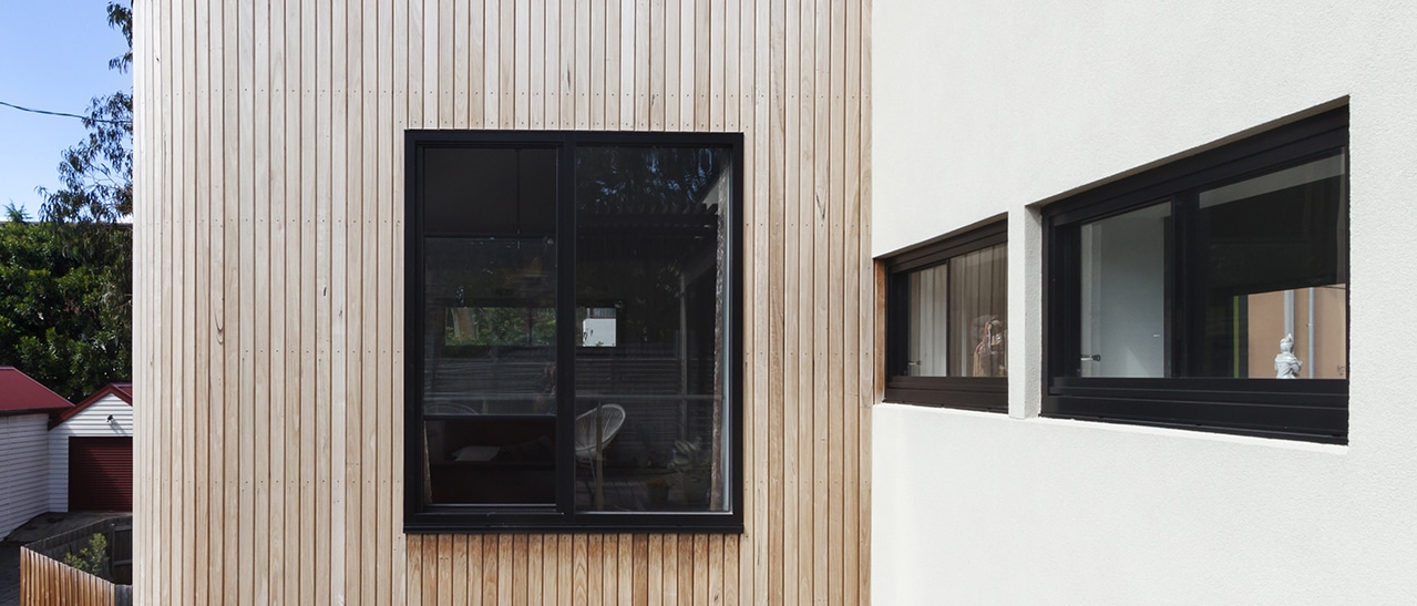 Schwarze Fenster eingebaut in Holzverschallung und VWS-System modernes Haus mit Holzfassade und verputzter Wand mit dunklen Fensterrahmen.