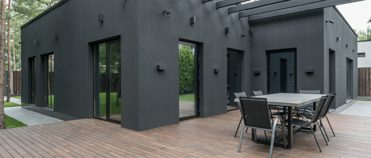 Ein modernes Haus mit dunkler Fassade, großen schwarzen Fenstern und Holzterrasse. Das Bild zeigt mögliche Auswirkungen dunkler Fensterfarben, die mehr Wärme aufnehmen und so potenziell zu Rahmenverzug führen können.