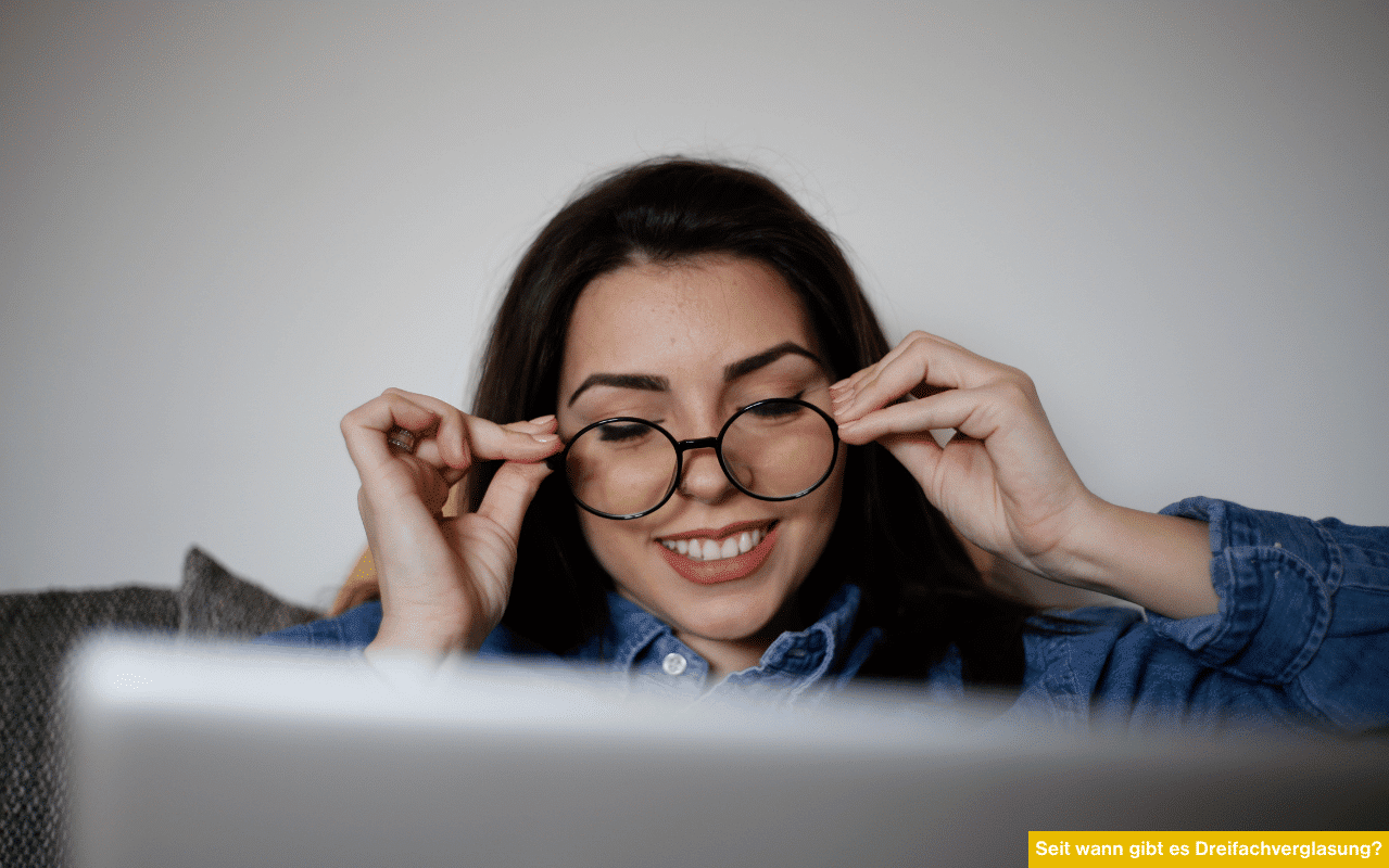 Seit wann gibt es Dreifachverglasung Junge Frau mit Brille liest auf Laptop über energieeffiziente Fensterentwicklung