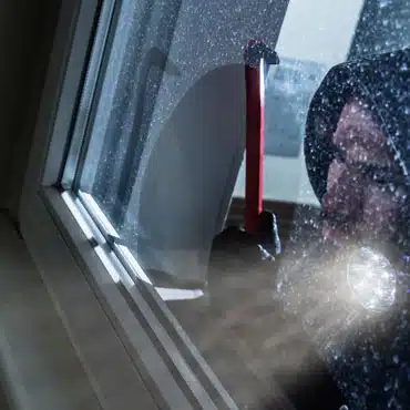 Ein Einbrecher versucht, ein Kellerfenster mit einer Brechstange zu öffnen. Sicherheit Kellerfenster ist besonders wichtig.