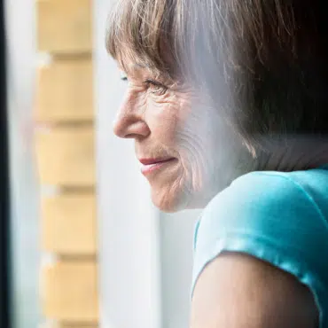 Sicherheitsfenster Österreich – Frau im Profil blickt entspannt und sicher aus dem Fenster ihrer Wohnung