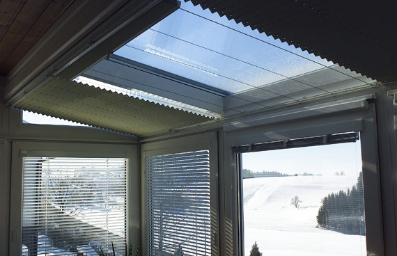 Innenansicht eines Wintergartens mit Plissees im Dachbereich und horizontalen Jalousien an den Seitenwänden.
