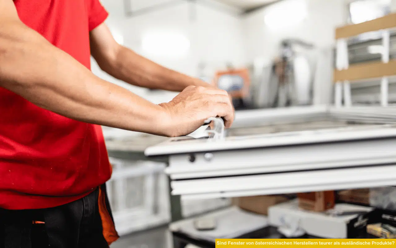 Ein Monteur arbeitet an einem weißen Fensterrahmen in einer Werkstatt, im Vordergrund sind Hände und Werkzeug zu sehen.