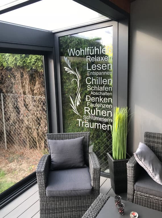 Innenansicht einer Lounge-Ecke im Sommergarten mit Polstermöbeln und bedruckter Glasscheibe.