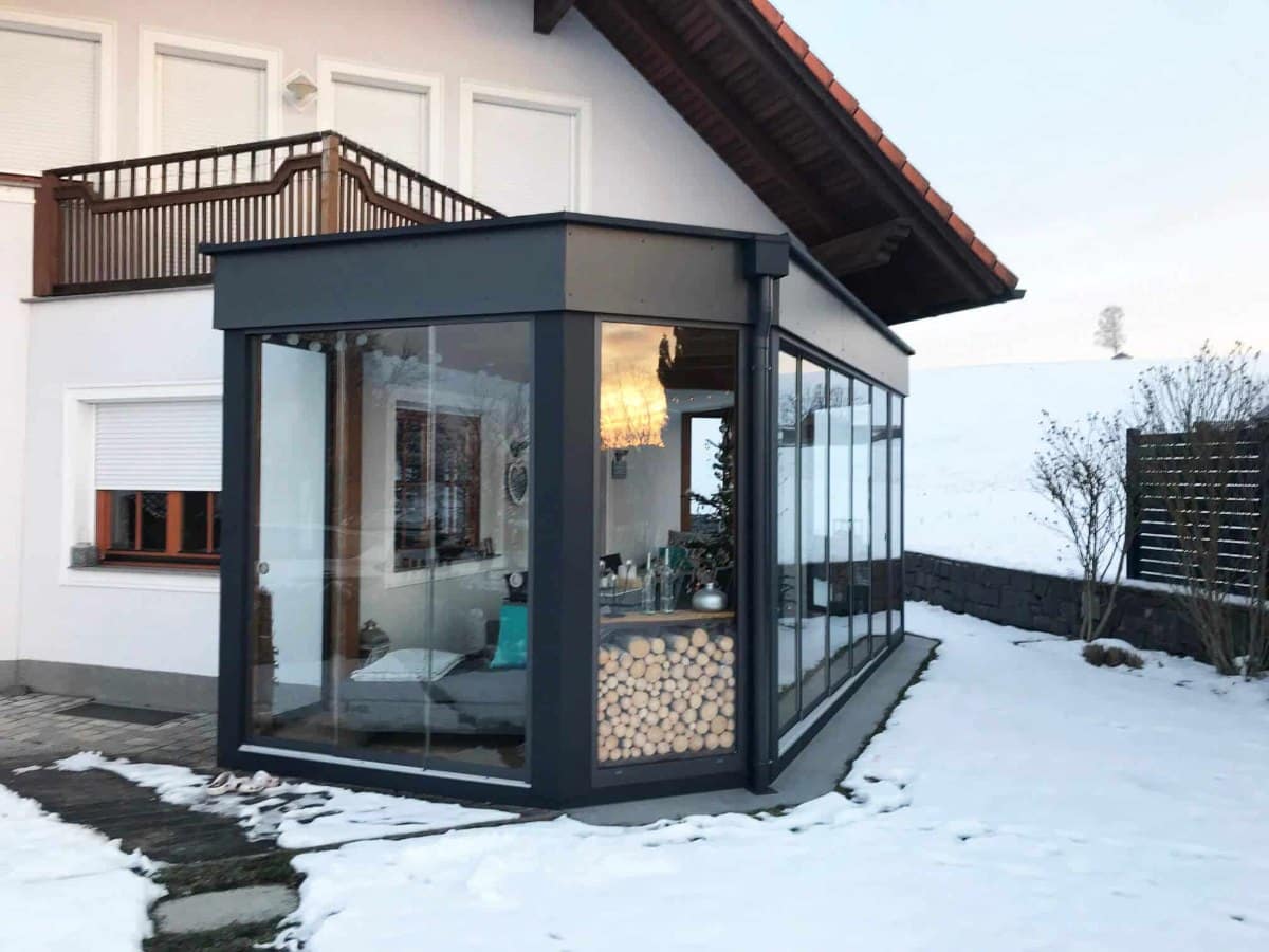 Sommergarten aus Aluminium mit Flachdach in Anthrazit und Ganzglas-Schiebetüren aus ESG an einem Einfamilienhaus im Winter