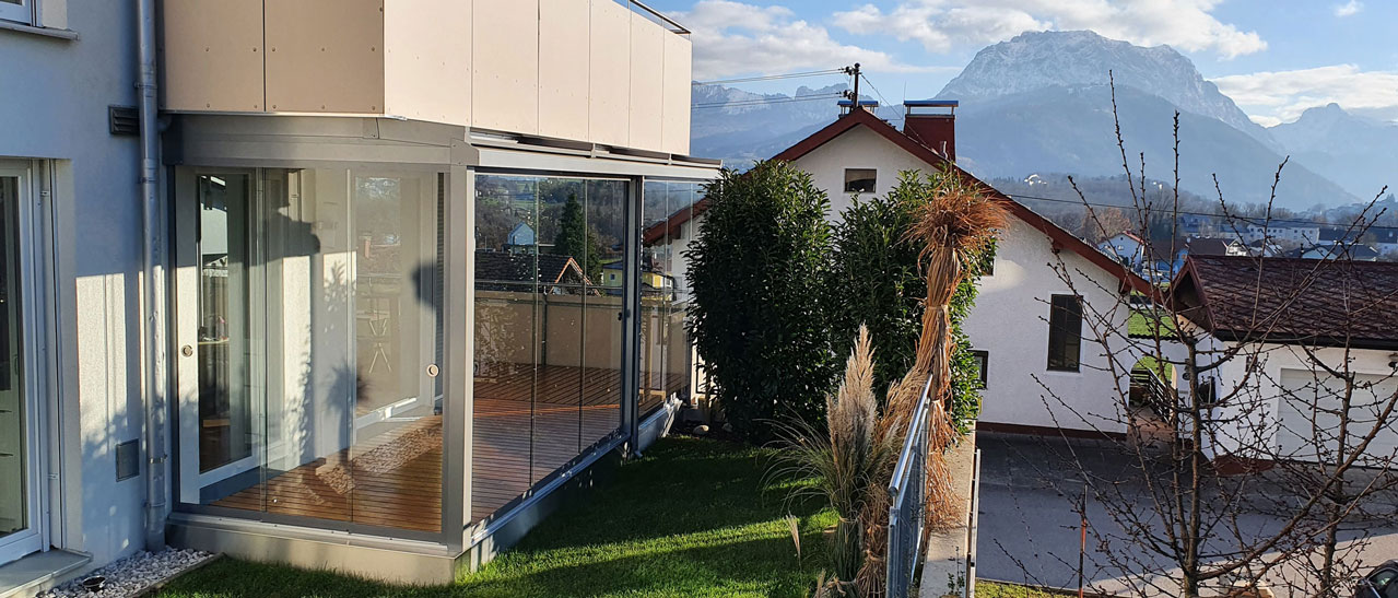 Sommergarten Erfahrungen zeigen: Glas-Schiebeelemente ermöglichen windgeschützte Terrassennutzung mit freiem Blick auf Natur und Berge