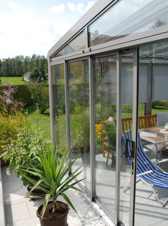 Aluminium-Sommergarten seitliche Verglasung schützt Terrasse vor Wind und Wetter bei freiem Blick ins Grüne