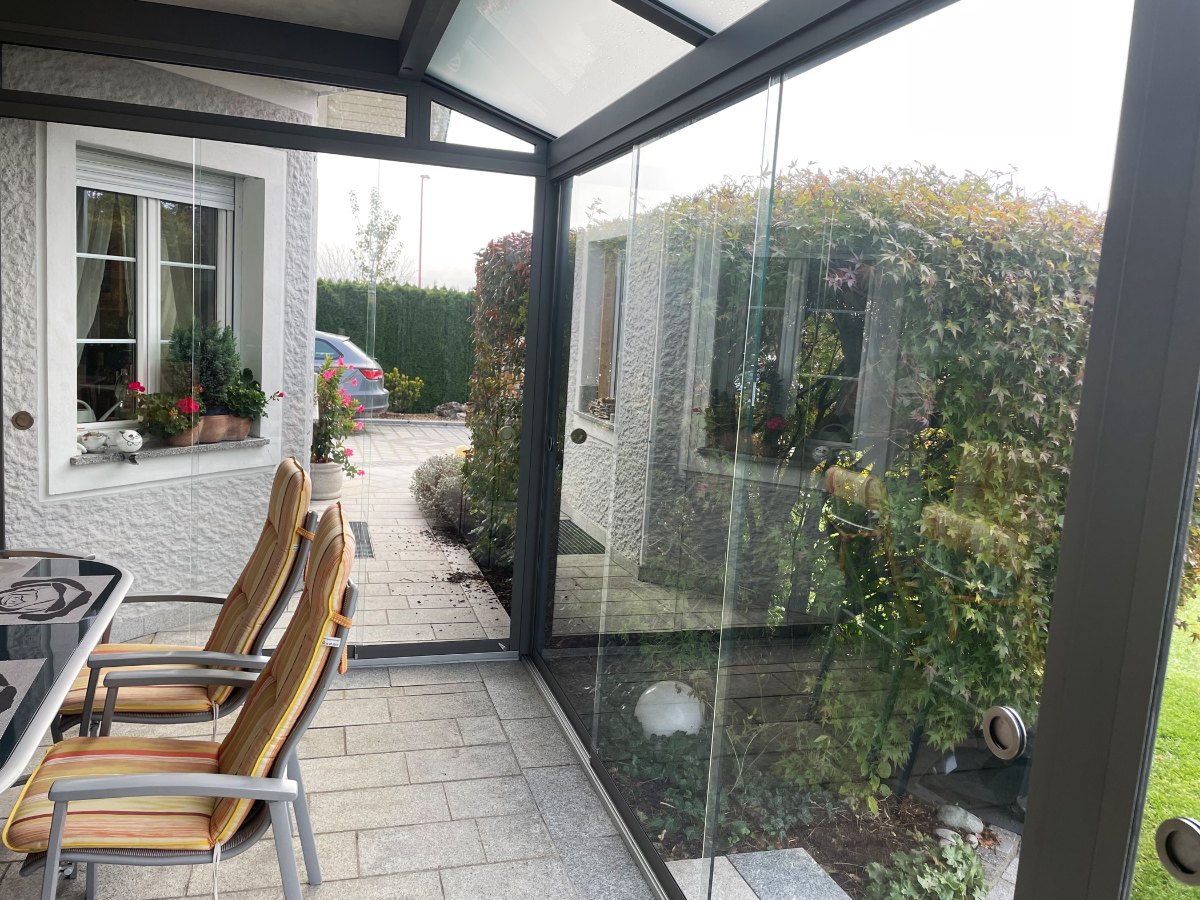 Ganzglas-Schiebeelemente aus 10 mm ESG schließen einen Sommergarten, der unter einem Balkon montiert ist