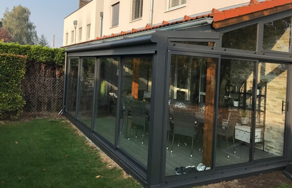 Außenansicht eines Aluminium-Sommergartens in Österreich mit Glasschiebewänden und passendem Ziegeldach von Wintergartenfirma Schmidinger.