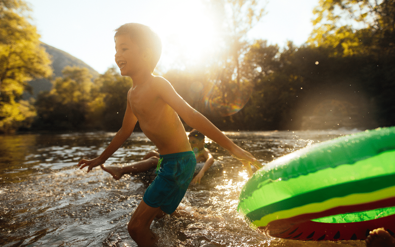 Sommerpause bei Fenster-Schmidinger mit fröhlichen Kindern beim Baden im Fluss unter strahlender Sommersonne in der Natur.