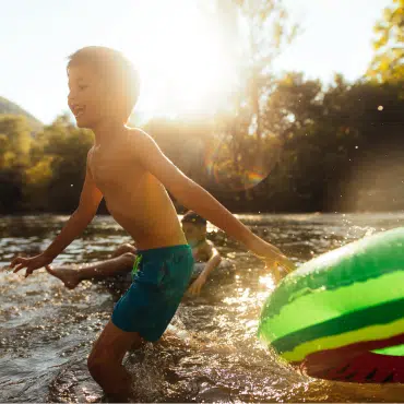 Sommerpause bei Fenster-Schmidinger symbolisiert durch spielende Kinder im Wasser bei Sonne und Natur in der Urlaubszeit.