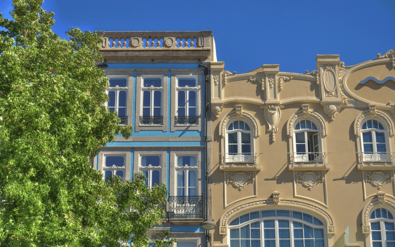 Sonderformen und Architekturfenster in der Praxis. Zwei historische Gebäude mit großen Architekturfenstern, kunstvollen Fassaden und Rundbogenformen neben einem grünen Baum im Vordergrund.