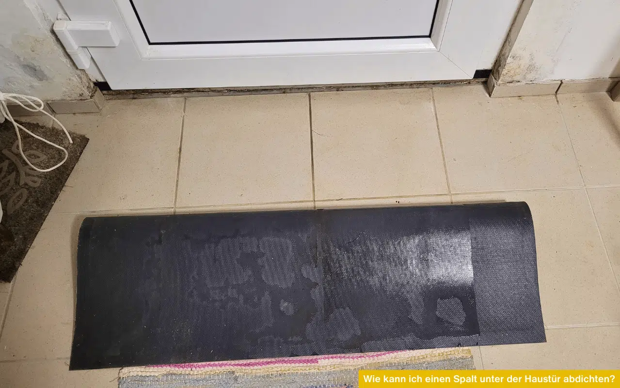 Innenansicht einer Haustürschwelle mit einem davor liegenden Gummischutz; zeigt Feuchtigkeitsspuren im Wandbereich.