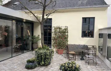 Ein gemütlicher Innenhof mit antiken Metallmöbeln und vielen Pflanzen; die Fenster des hellen Hauses sind durch nachträglich angebrachte dunkle Sprossen klassisch gegliedert.