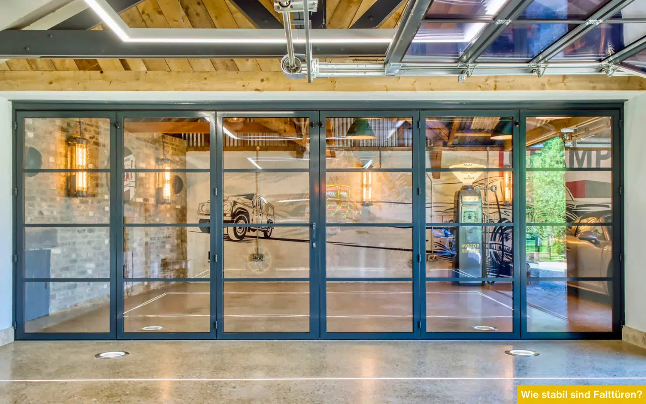 Große Glas-Falttür mit dunklem Aluminiumrahmen in einer modern gestalteten Garage mit Industrie-Elementen.
