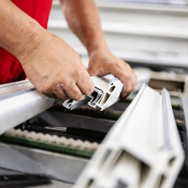 Nahaufnahme eines Technikers, der eine Metallverstärkung in ein weißes Kunststoff-Fensterprofil einsetzt.