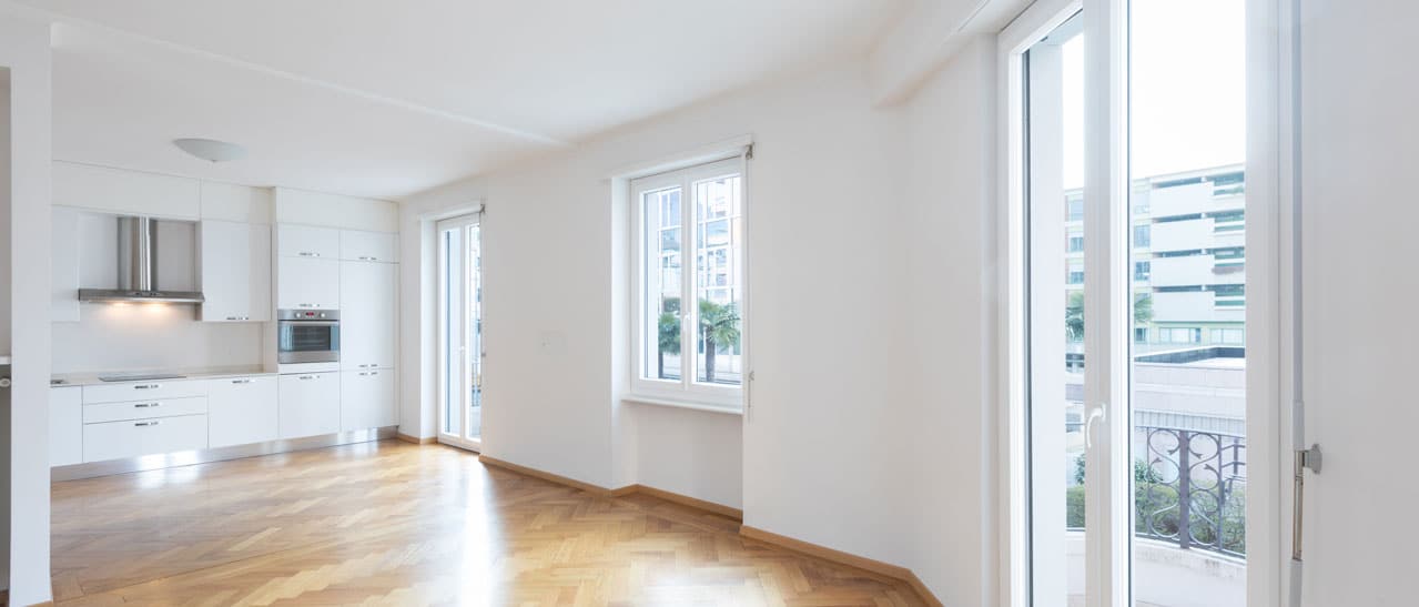 In einem modernen Wohnraum mit Parkettboden sind große Stulpfenster und Balkontüren zu sehen.