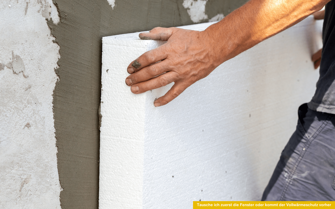 Ein Handwerker bringt eine weiße Dämmplatte an einer Hauswand an - Symbol für Wärmeschutz und energetische Sanierung.