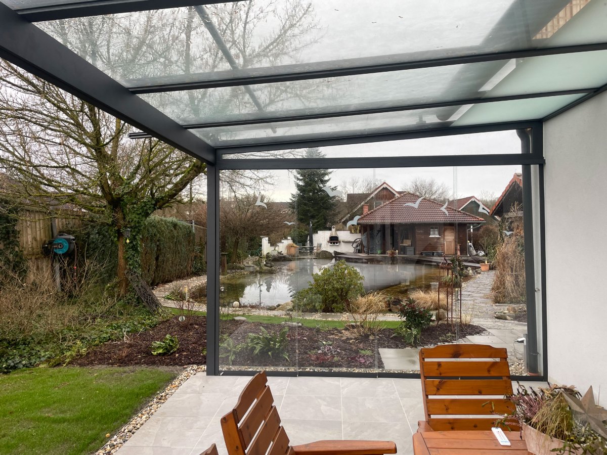 Terrassenüberdachung in RAL 7016 Anthrazitgrau mit satiniertem Glasdach und Blick in den Garten mit Teich in Scharten