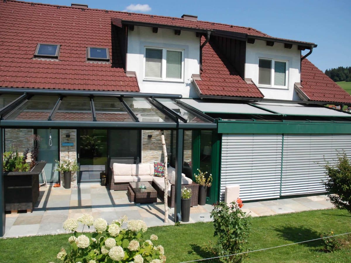 Terrassenüberdachung aus Aluminium mit Glasdach an einem Einfamilienhaus mit Ziegeldach