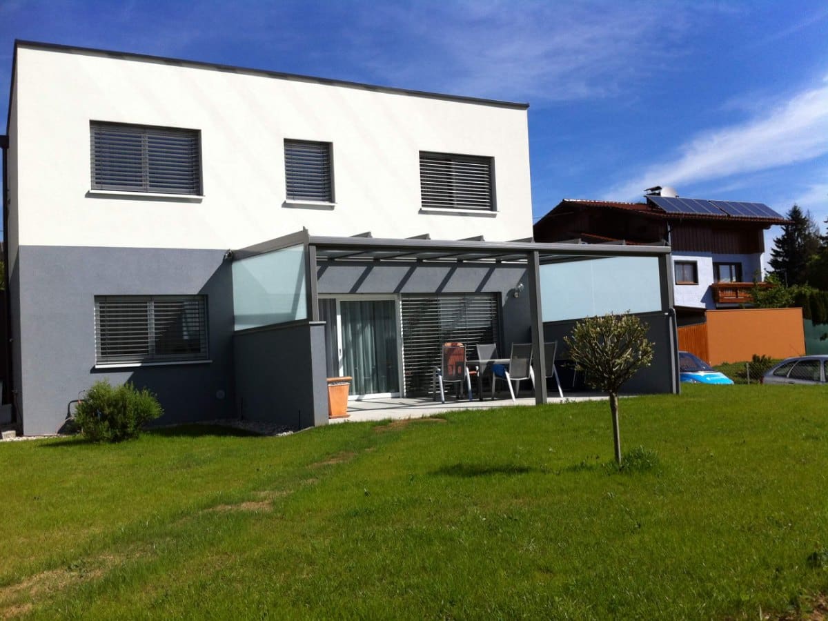 Terrassenüberdachung in RAL 9007 Graualuminium mit satiniertem Glas-Seitenteil an einem modernen Haus mit Flachdach