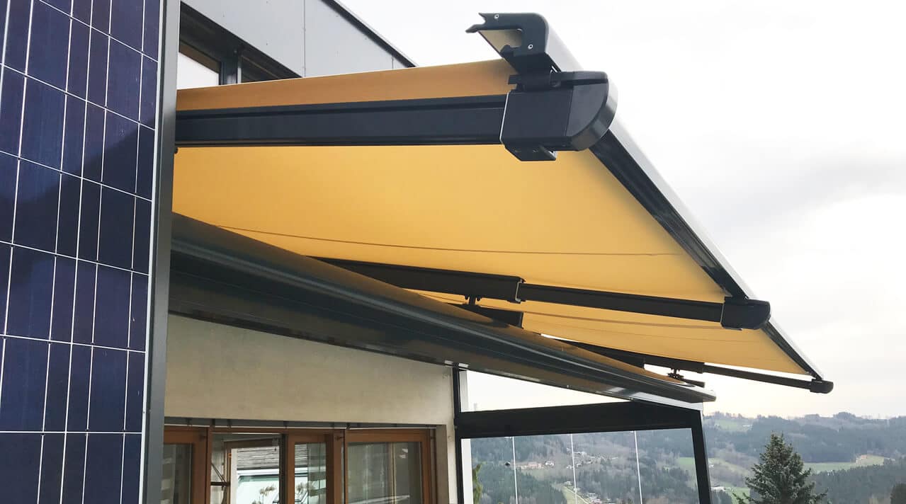 Ausgefahrene Markise an einer Terrassenüberdachung, montiert an der Hausfassade mit freiem Blick ins Umland in Österreich.