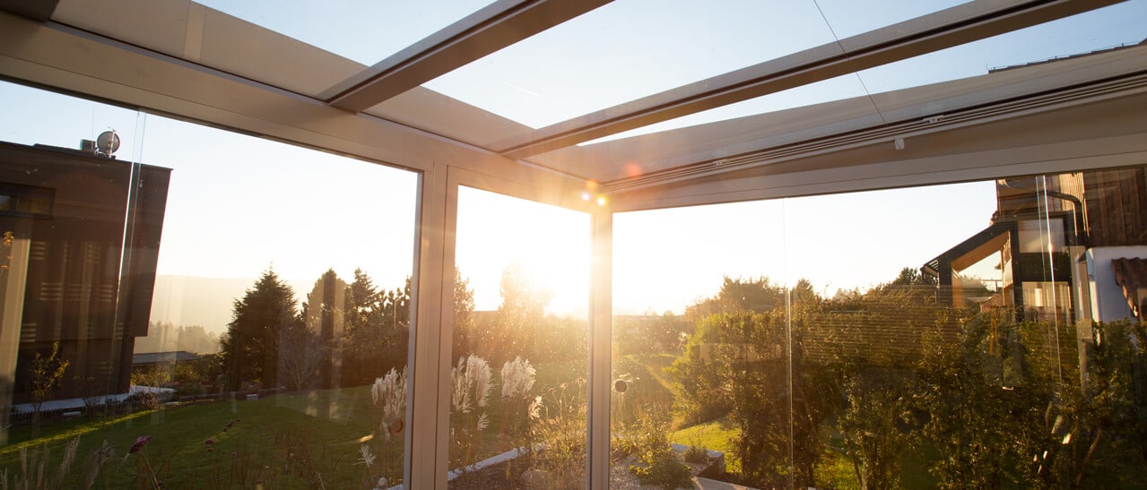 Glasüberdachung mit Blick auf Garten bei Sonnenuntergang zeigt Terrassenüberdachungen optimal überdacht