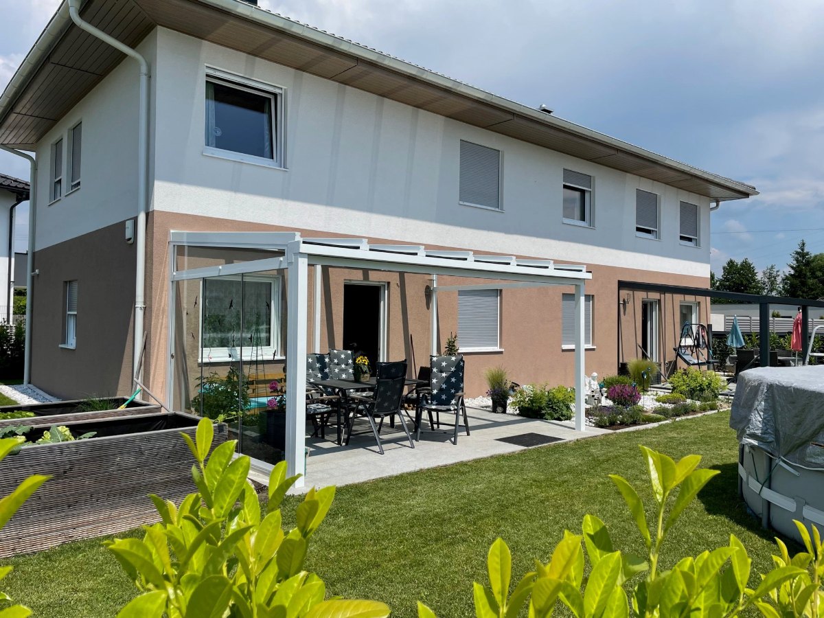 Helle Terrassenüberdachung aus Aluminium mit Glasdach und Seitenteil an einem Einfamilienhaus in Pupping