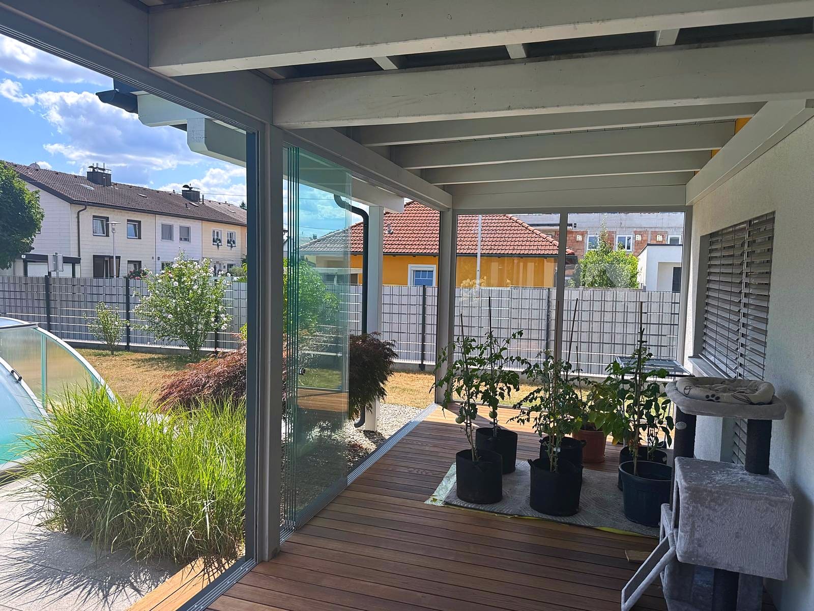 Geöffnete Ganzglas-Schiebeelemente einer Terrassenverglasung unter Holzkonstruktion mit Blick in den Garten in Pasching