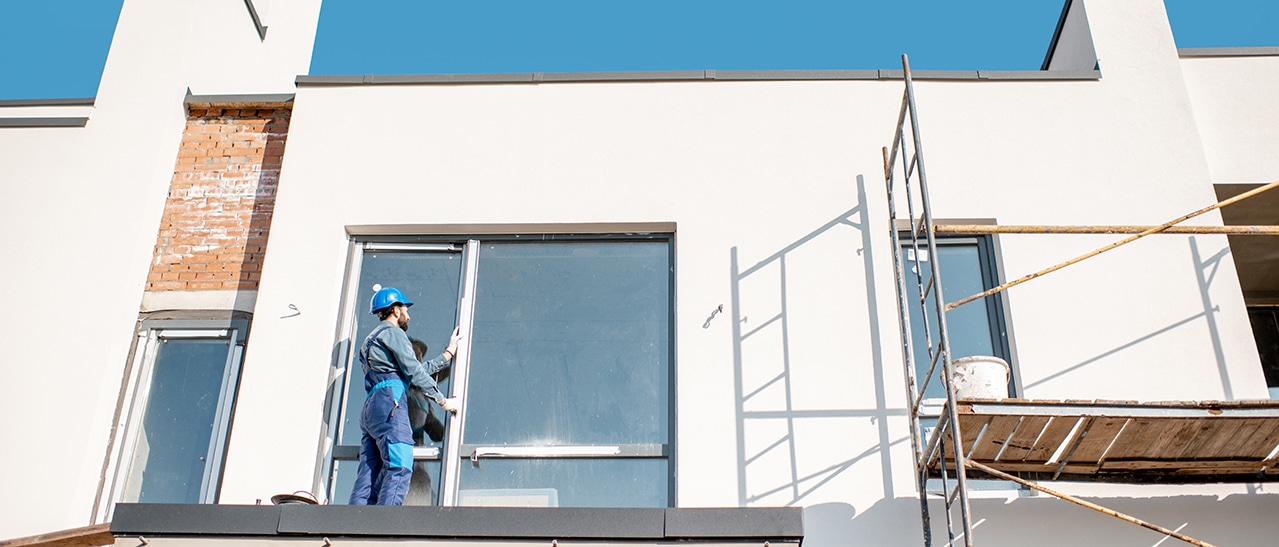 Tipps für die Fensterrenovierung – Arbeiter installiert Fensterrahmen an Neubau oder saniertem Gebäude mit Gerüst.