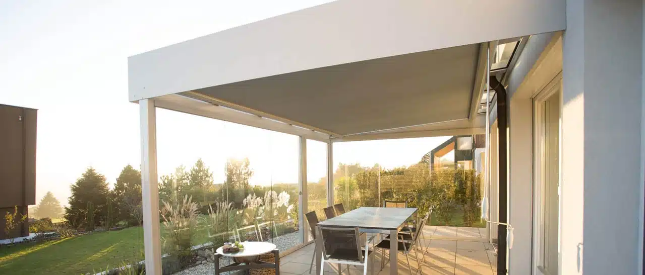 Unterglasmarkise als Sonnenschutz unter dem Glasdach einer Terrasse mit Blick in den Garten