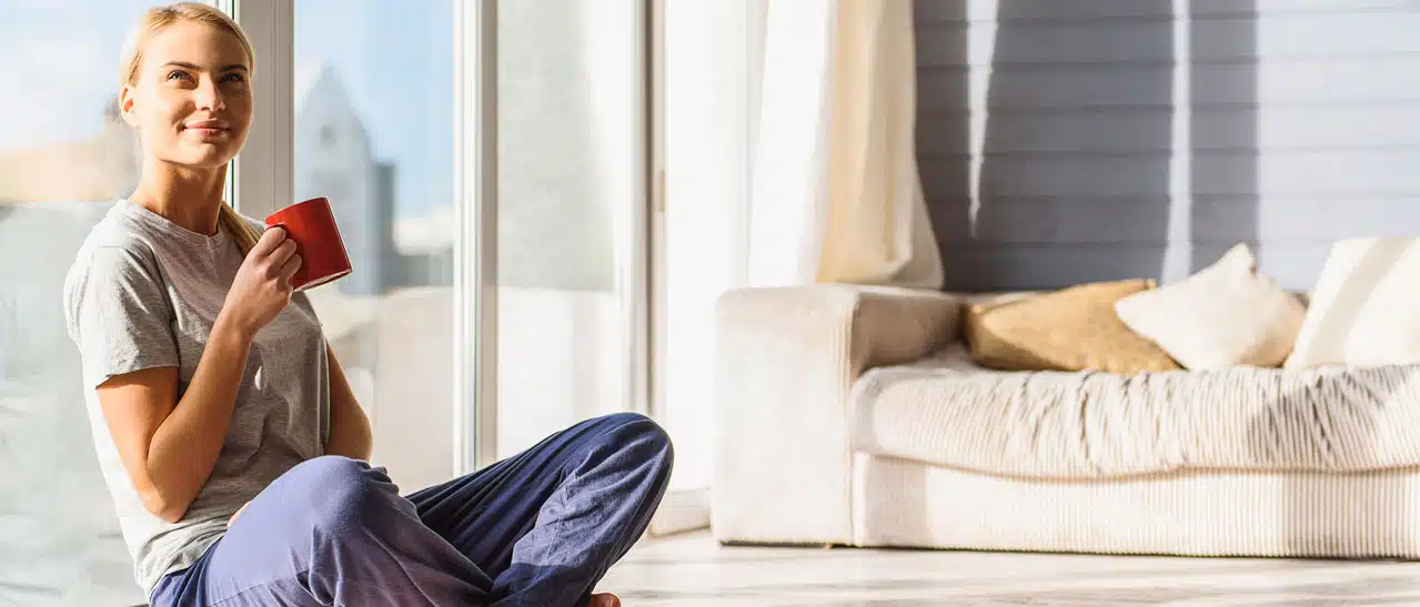 Fensterpreise sinken. Glückliche Frau sitzt 2023 in der Wohnung vor neuen Fenstern mit guten Preisen.