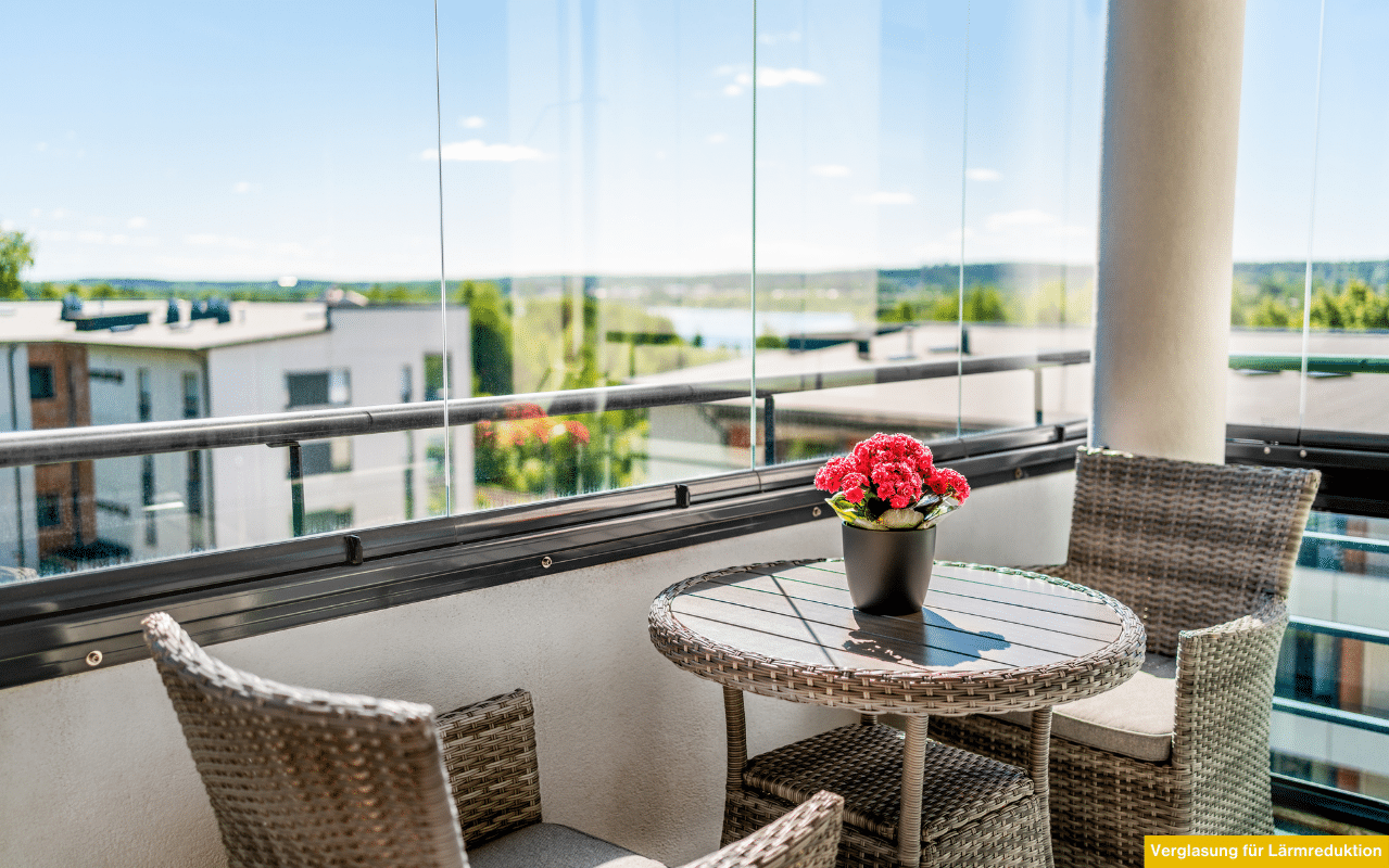 Verglaster Balkon mit Sitzgruppe und Blume als Beispiel für Verglasung für Lärmreduktion in städtischen Wohngebieten.