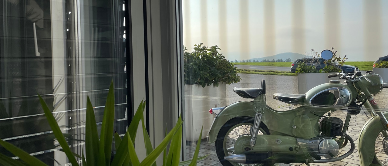 Vogelschutzglas für Mehrfachverglasung moderne Fensterfront mit reflektionsarmen Scheiben und Ausblick auf Oldtimer-Motorrad und Landschaft.