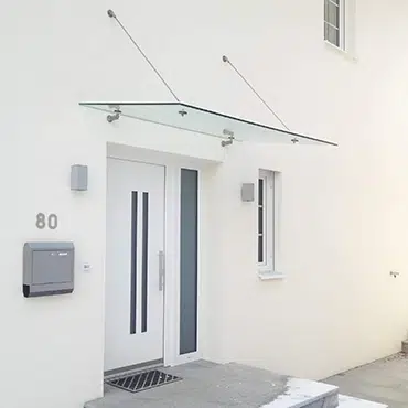 Vordach aus Glas nach Maß über weißer Eingangstür – passgenaue Lösung für moderne Fassadengestaltung