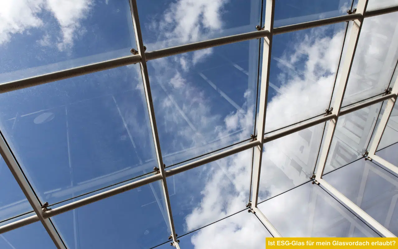 Blick durch eine moderne Glasdachkonstruktion aus Sicherheitsglas gegen den blauen Himmel mit weißen Wolken.
