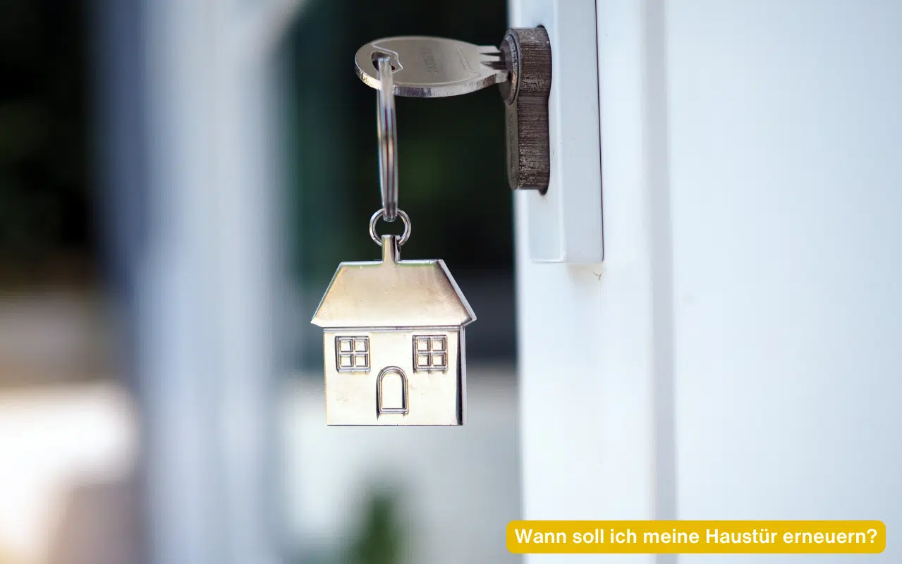 Wann soll ich meine Haustür erneuern? Schlüssel mit Hausanhänger steckt im Schloss einer weißen modernen Haustür