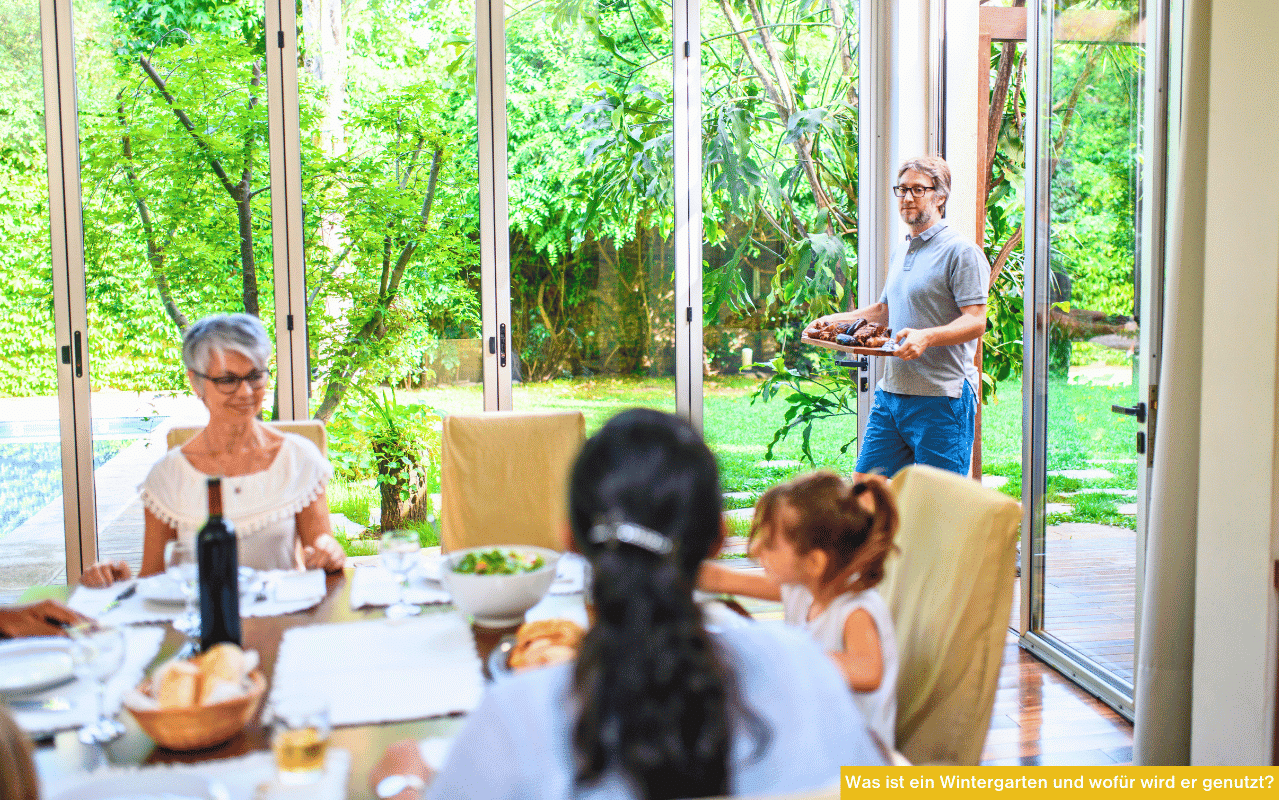 Was ist ein Wintergarten und wofür wird er genutzt zeigt Familie beim Essen in hellem Raum mit großen Glasflächen zum Garten