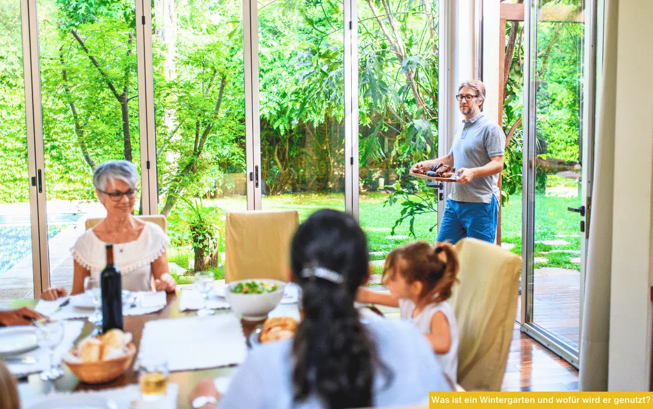 Was ist ein Wintergarten und wofür wird er genutzt zeigt Familie beim Essen in hellem Raum mit großen Glasflächen zum Garten