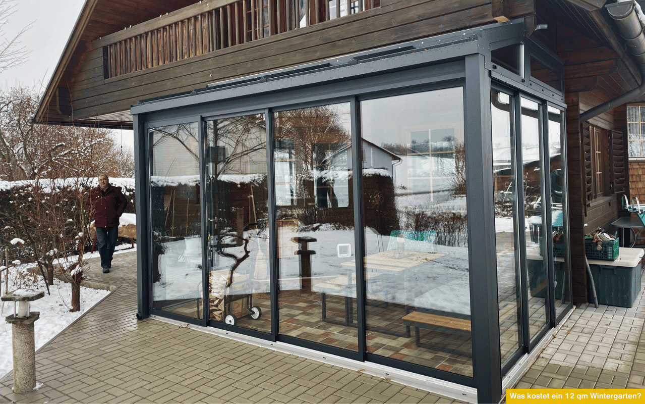 Was kostet ein 12 qm Wintergarten? Moderner, verglaster Wintergarten im Schnee mit Schiebetüren, Pultdach und angrenzendem Holzhaus.