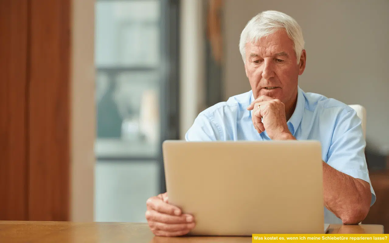 Was kostet es, wenn ich meine Schiebetüre reparieren lasse? Senior vergleicht Reparaturpreise am Laptop im Wohnraum.