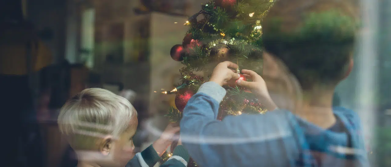 Kinder dekorieren Weihnachtsbaum hinter klarem Fensterglas sichtbar, festliche Stimmung.