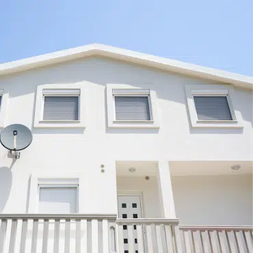 Weiße Hausfassade mit mehreren Fenstern und geschlossenen grauen Rollladen. Sicht- und Sonnenschutz für das Eigenheim.