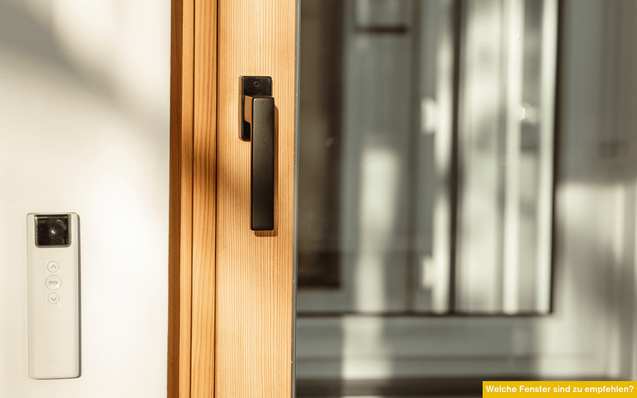Nahaufnahme eines modernen Holzfensters mit schwarzem Griff. Sonnenlicht fällt auf den Fensterrahmen, im Hintergrund ist eine verglaste Fläche sichtbar.