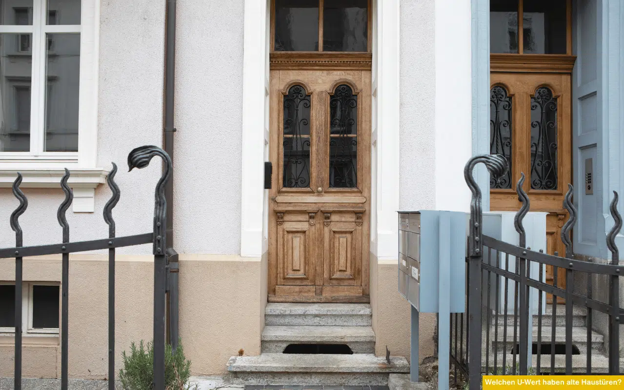Das Bild zeigt eine alte Holzhaustür mit dekorativen Eisen-Gittern, flankiert von Hausfassaden und Briefkästen. Sie symbolisiert typische ältere Eingangstüren mit schlechter Wärmedämmung in Altbauten.