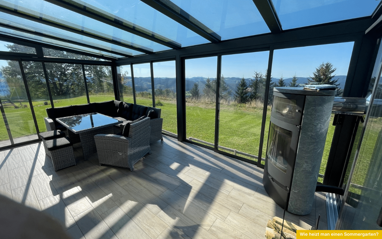 Ein moderner Sommergarten mit Panoramablick und Glaswänden, eingerichtet mit gemütlicher Sitzgruppe und einem Kaminofen, der an kühlen Tagen für wohlige Wärme sorgt.