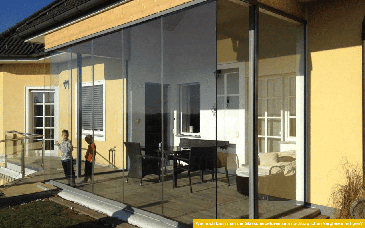 Ein modernes Einfamilienhaus mit nachträglich verglaster Terrasse durch große Glasschiebetüren. Zwei Kinder stehen vor der Glasfront.
