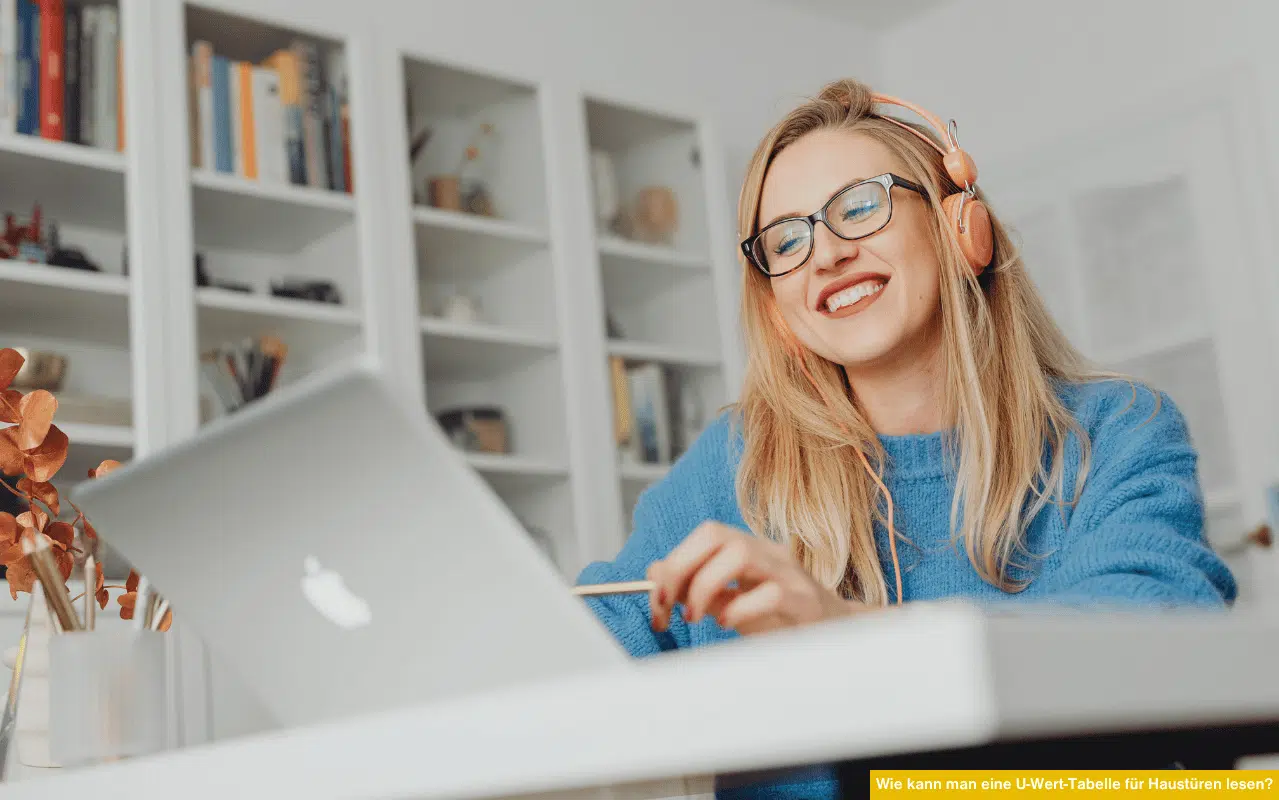 ine junge Frau trägt Kopfhörer und lächelt, während sie an einem Laptop sitzt. Das Motiv steht symbolisch für das digitale Informieren über Energieeffizienz und das Verständnis von U-Wert-Tabellen bei Haustüren.