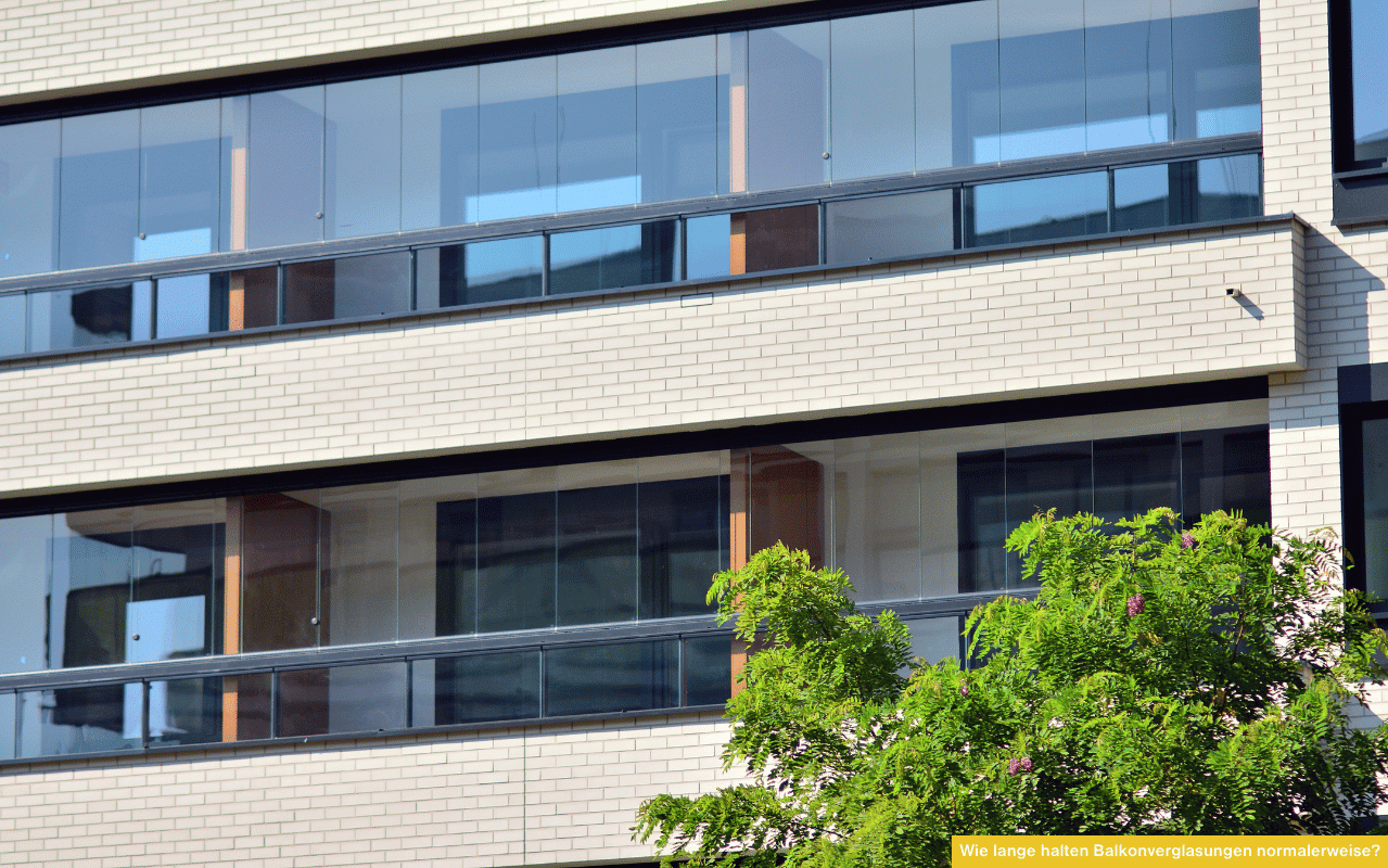 Wie lange halten Balkonverglasungen normalerweise? Blick auf moderne, rahmenlose Balkonverglasung an einem Mehrparteienhaus.